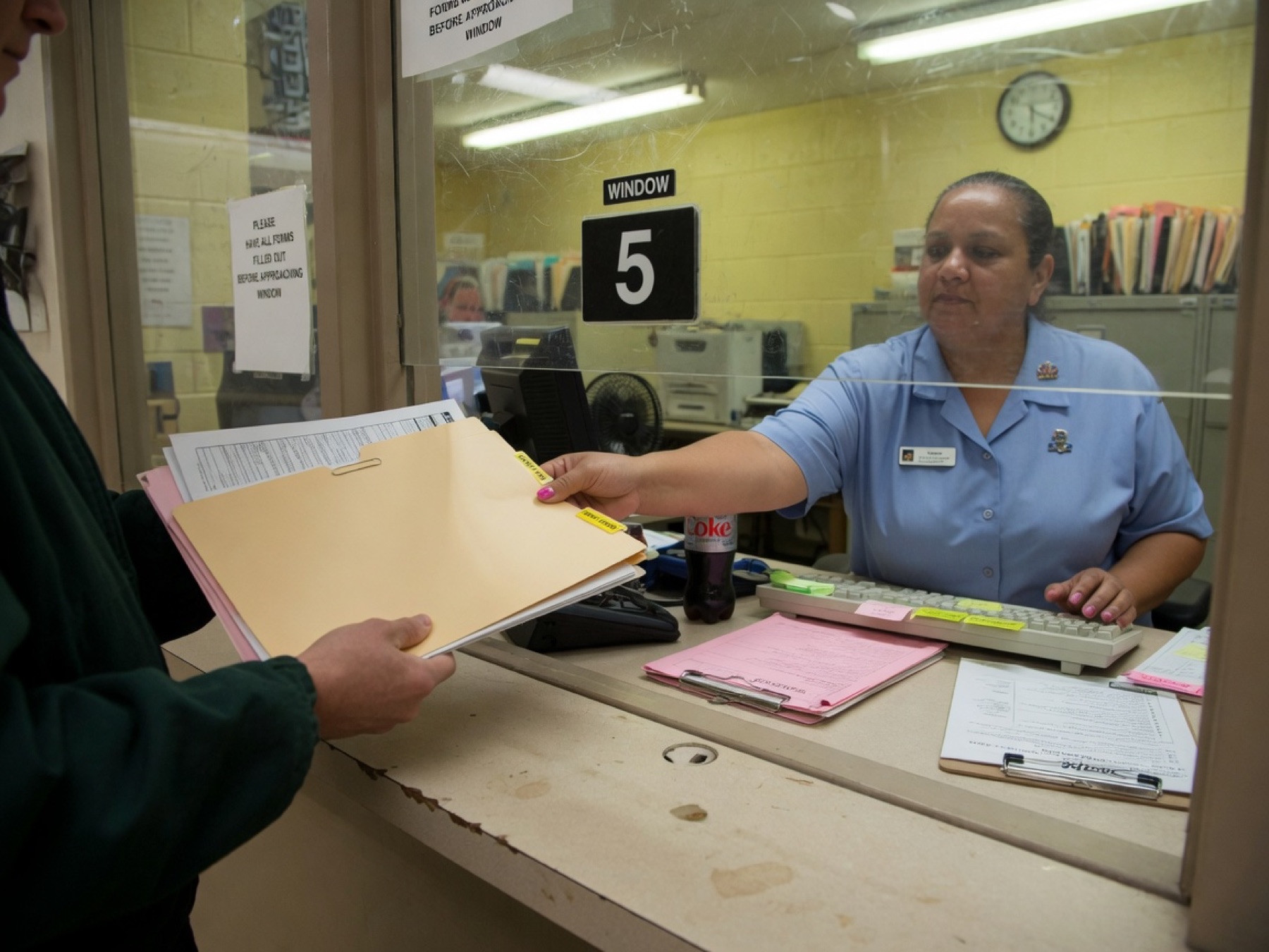 A visitor handing a folder of forms to a clerk at DMV window 5.
